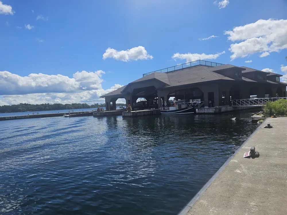 The Thousand Islands Boat Museum, a large dark boathouse-style building on the Gananoque waterfront, seen across the water.