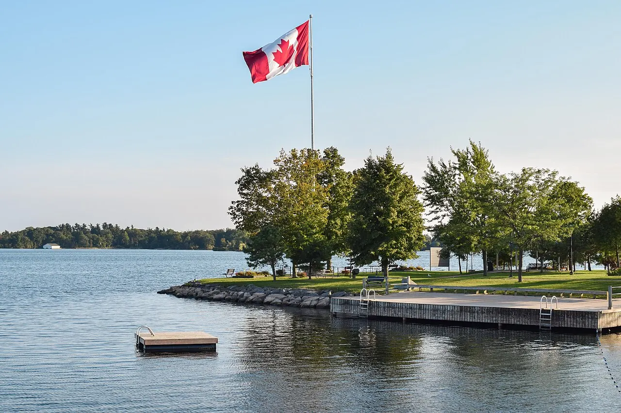 The swim dock and lawn at Joel Stone Park on the St. Lawrence River, with a Canadian flag flying above the trees.
