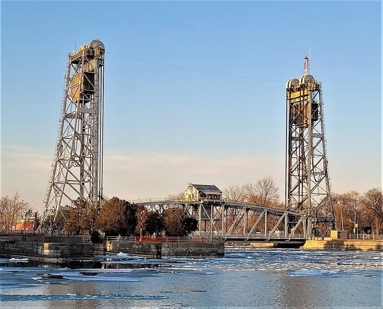 The twin towers of the Clarence Street lift bridge over the Welland Canal in Port Colborne at sunset, with ice on the water.