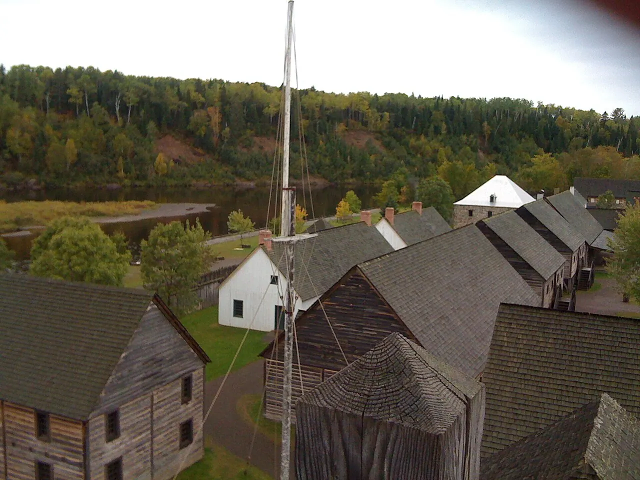 Log buildings inside the palisade at Fort William Historical Park, seen from above with a flagpole in the foreground.